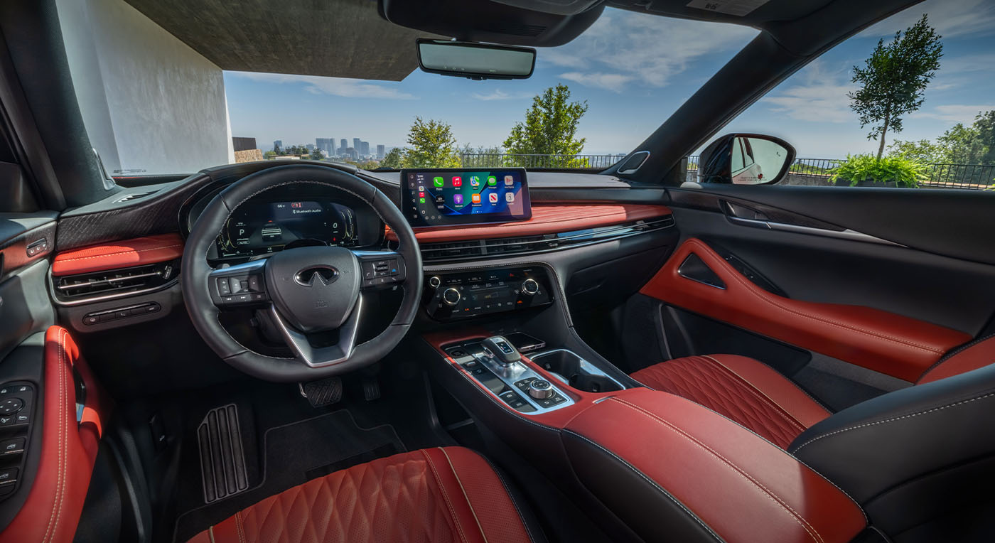 Luxurious car interior of Infiniti QX65 with red leather seats and a sleek dashboard featuring a large touchscreen. The city skyline is visible through the windshield.